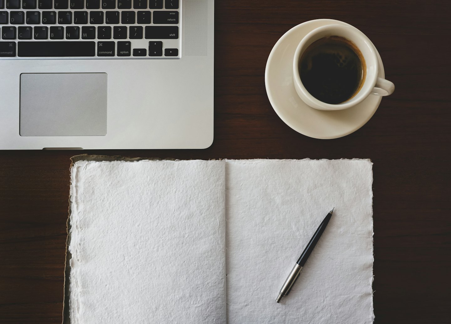 Computer portatile e caffè su una scrivania di legno scuro.